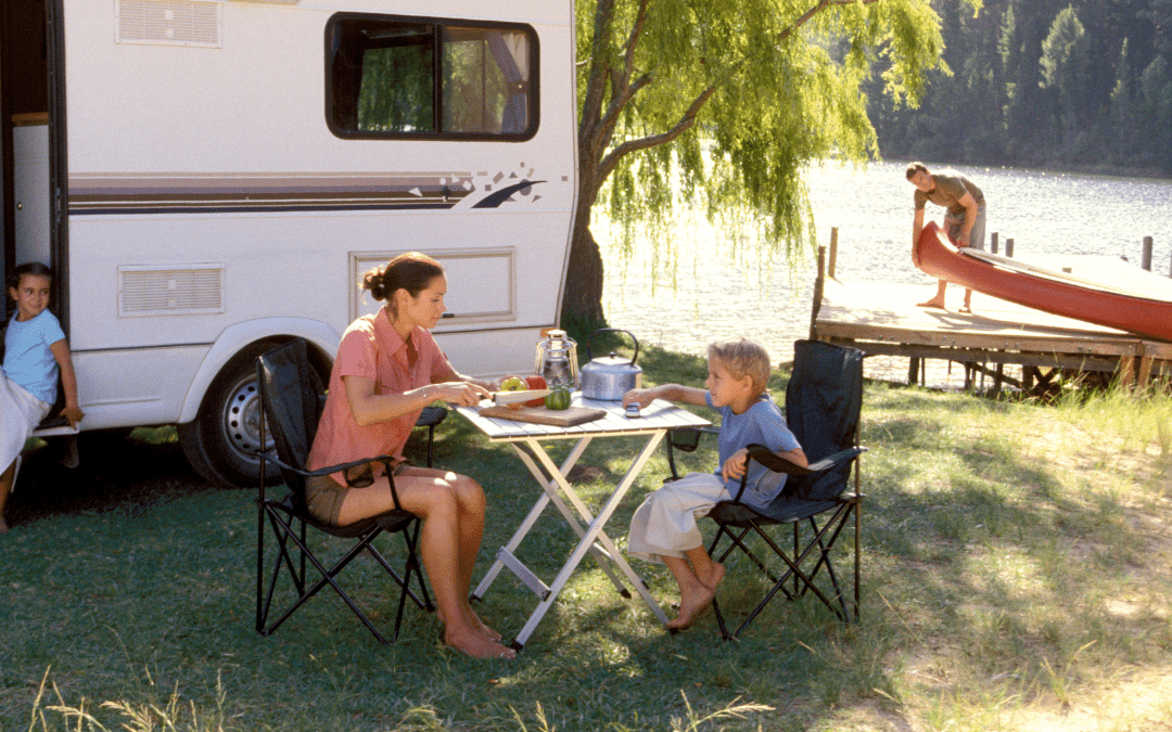 Happy family enjoying a camping meal outside their RV at a scenic lakeside location
