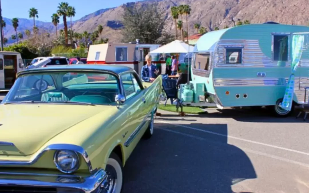 Vintage turquoise travel trailer and classic yellow convertible car at an outdoor vintage trailer show in the desert