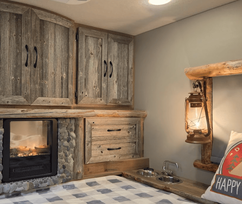 Custom horse trailer living quarters by Ace of Spades Custom RV featuring rustic weathered wood cabinets, stone electric fireplace, cozy bed, and pet-friendly details in Las Vegas