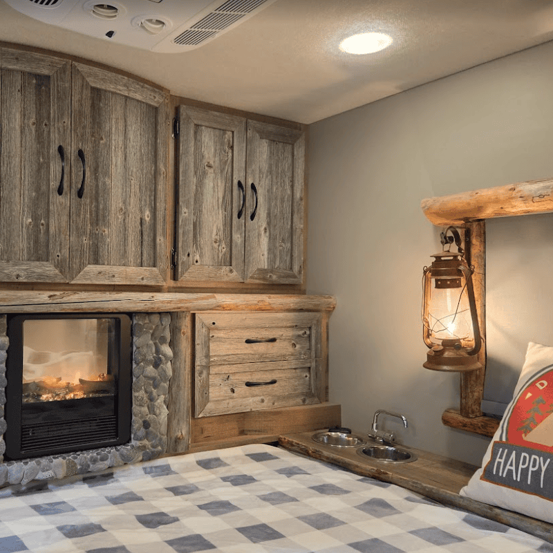 Custom horse trailer living quarters by Ace of Spades Custom RV featuring rustic weathered wood cabinets, stone electric fireplace, cozy bed, and pet-friendly details in Las Vegas
