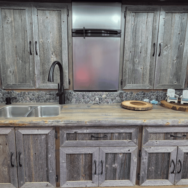 Custom horse trailer living quarters kitchen by Ace of Spades Custom RV with rustic weathered wood cabinets, stainless steel refrigerator, double sink, pebble stone backsplash, and wood countertop in Las Vegas