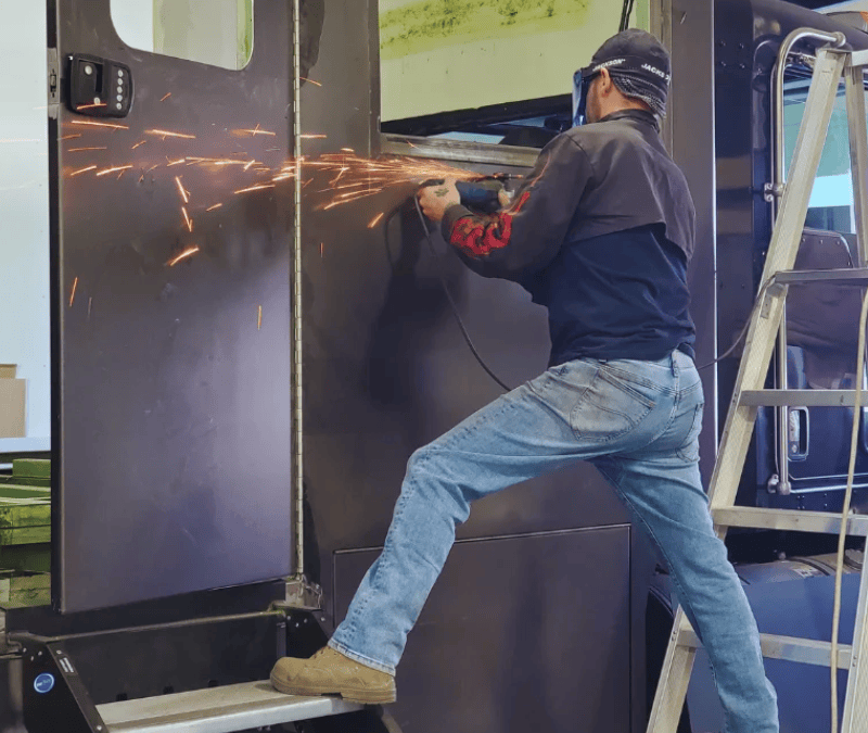 RV technician grinding and repairing metal panel on large RV exterior in Las Vegas workshop