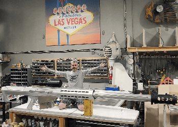 Builder of the Barrett Truck posing with a Barrett 50 caliber rifle in the workshop, highlighting the inspiration behind the custom 50 Caliber smoke stacks