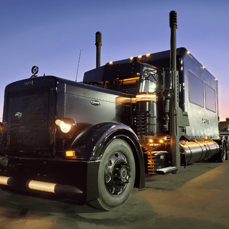 Black Barrett Truck custom 1998 Peterbilt conversion featuring handcrafted Barrett 50 Caliber smoke stacks and LED lighting at dusk