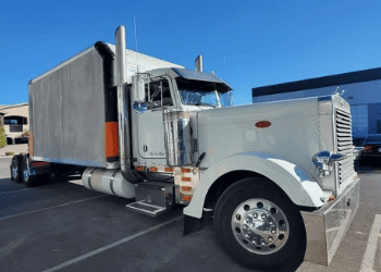 White Barrett Truck Peterbilt 379 custom build parked in sunlight showing chrome grille, dual exhaust stacks, and custom enclosed trailer